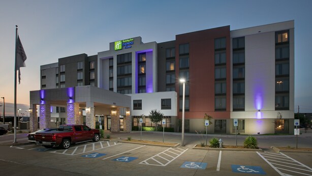 Un hotel Holiday Inn Express con estacionamiento, espacios accesibles para discapacitados y una camioneta pickup roja estacionada al frente.