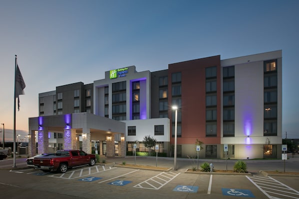 Un hotel Holiday Inn Express con estacionamiento, espacios accesibles para discapacitados y una camioneta pickup roja estacionada al frente.