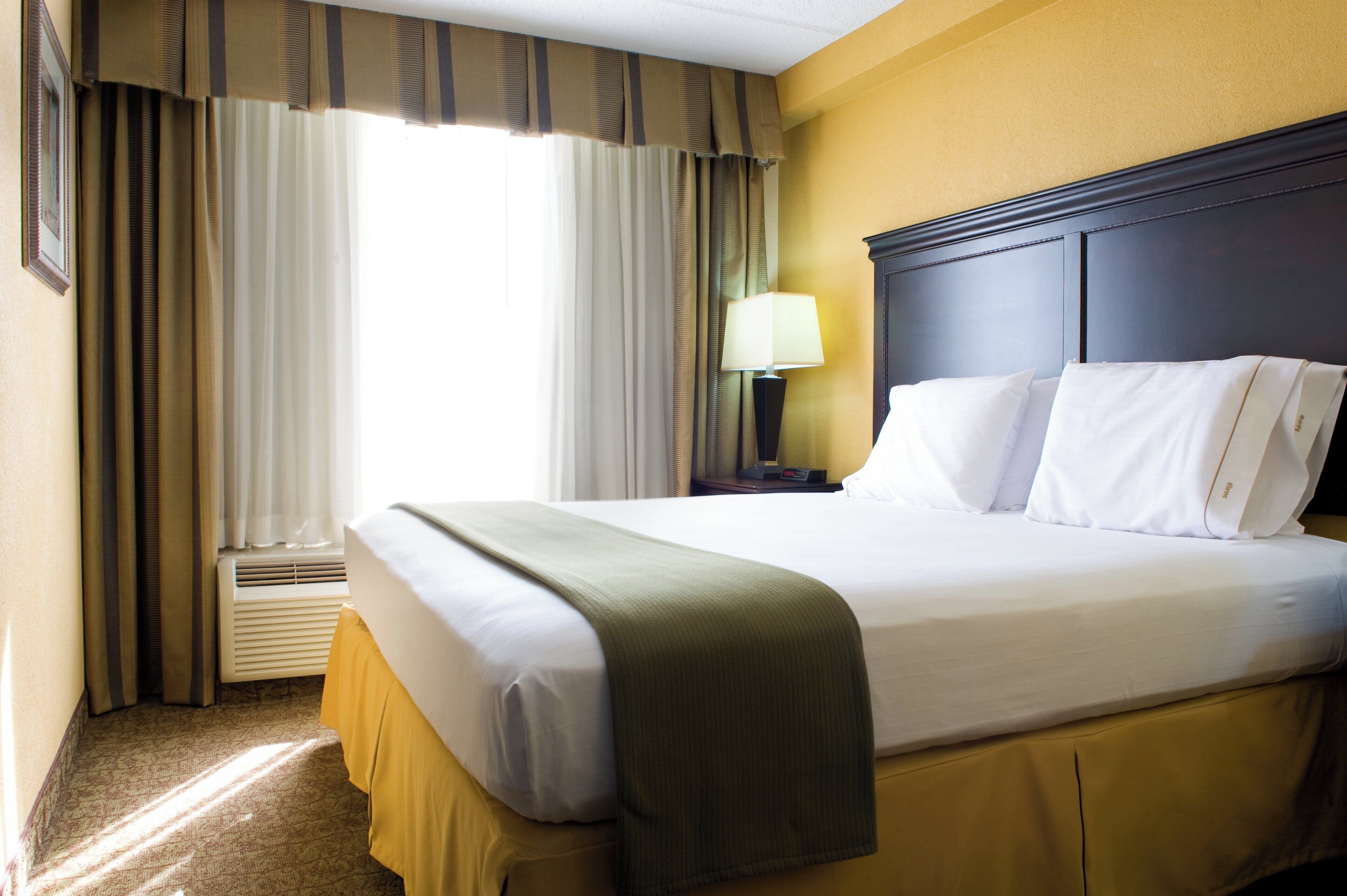 A hotel room with a bed, curtains, a lamp, and a window.