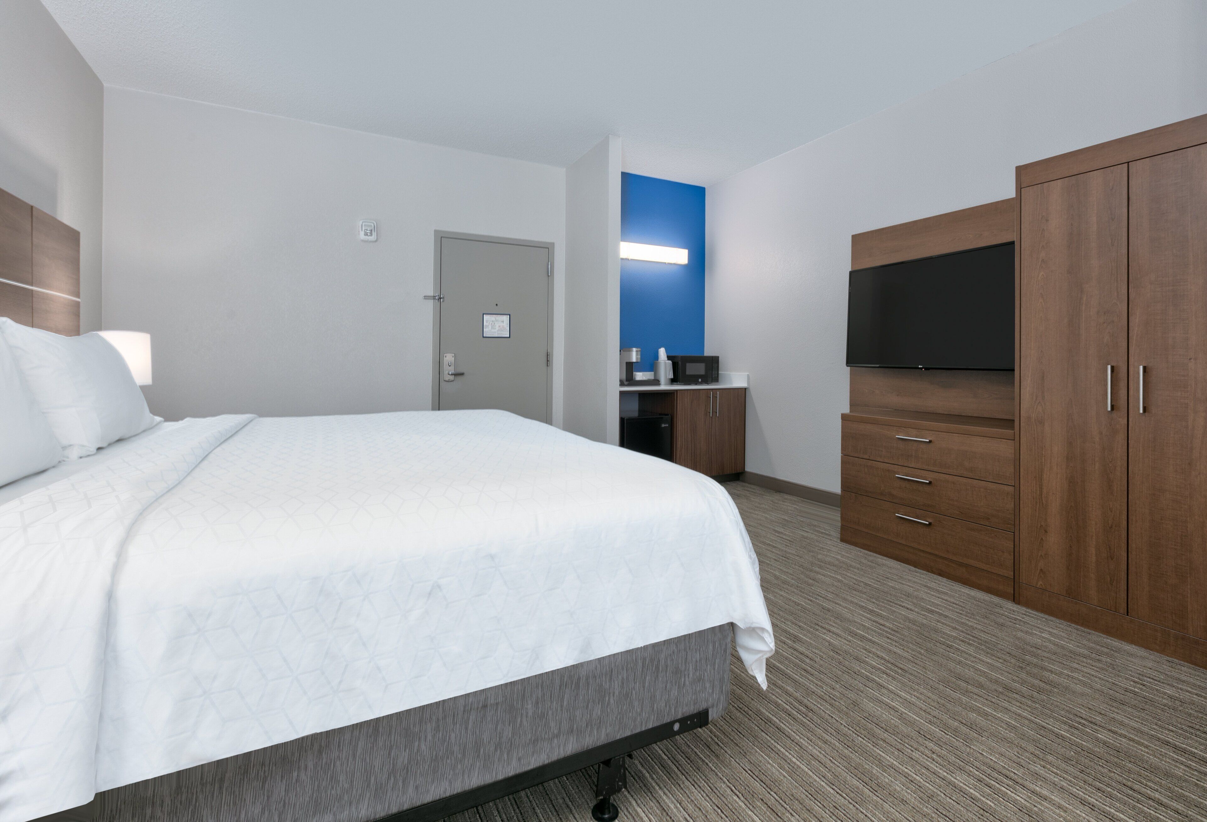A hotel room with a large bed, a TV, wooden wardrobe, and a desk with a microwave.