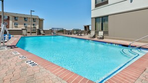 Una piscina rectangular con borde de azulejos, rodeada de sillones de descanso y una terraza de ladrillo.