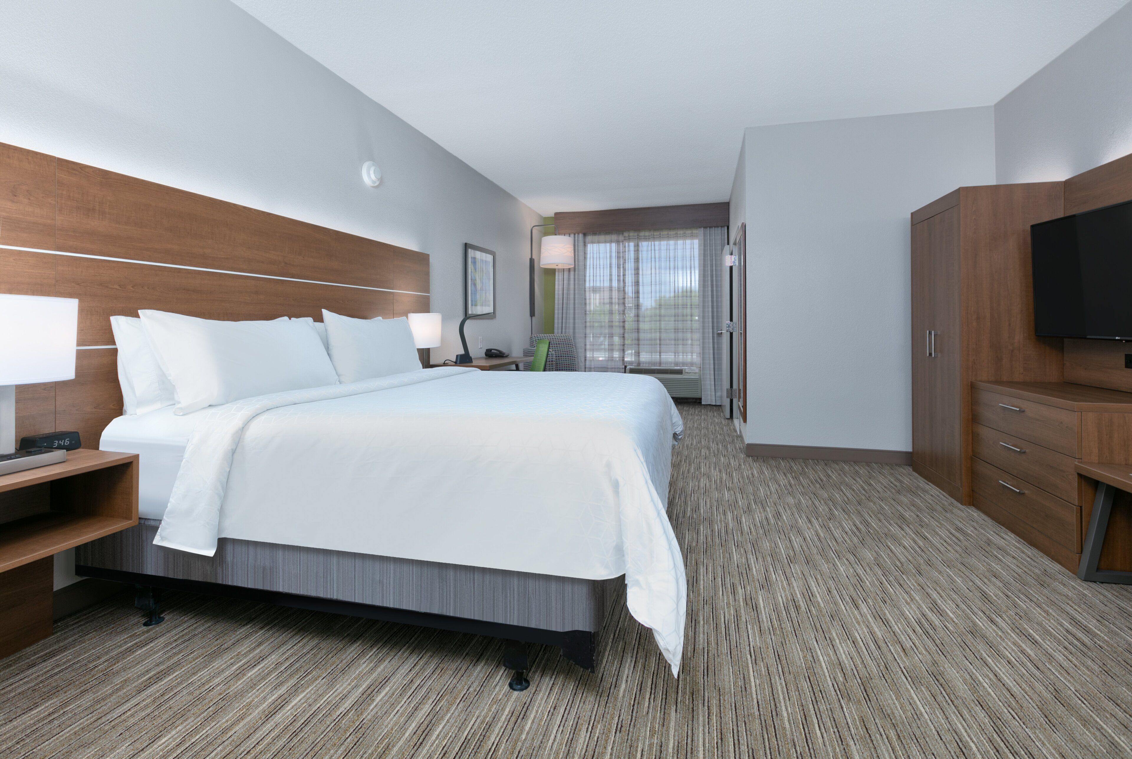 A hotel room with a large bed, a desk with a lamp, a flat-screen TV, and a wardrobe.