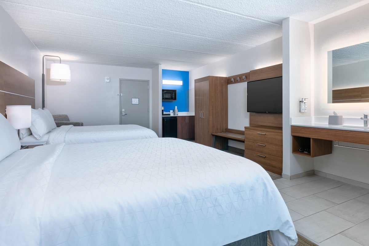A hotel room with two beds, a TV, a mirror, and a kitchenette.