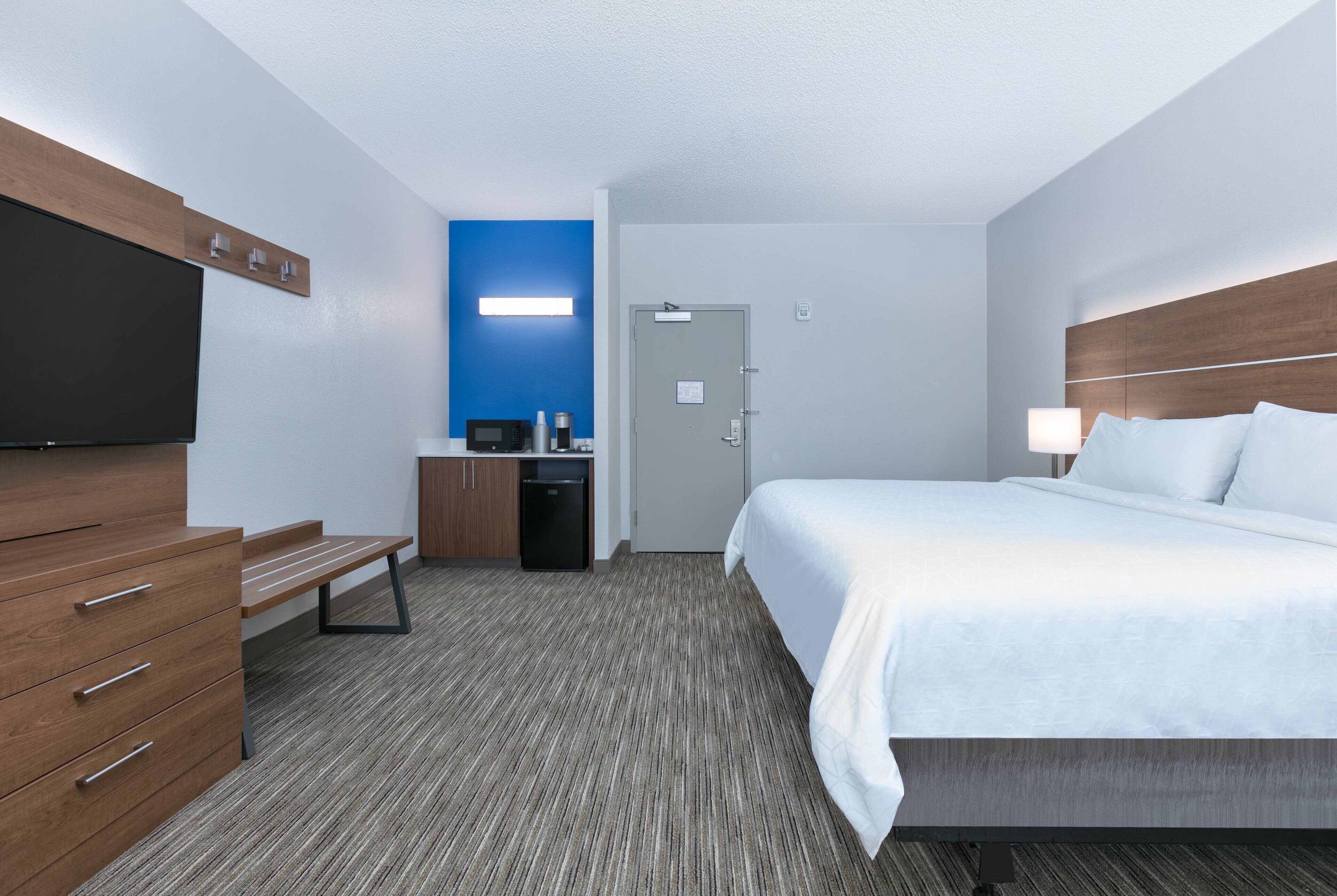 A hotel room with a bed, a desk, a television, and a small kitchenette.