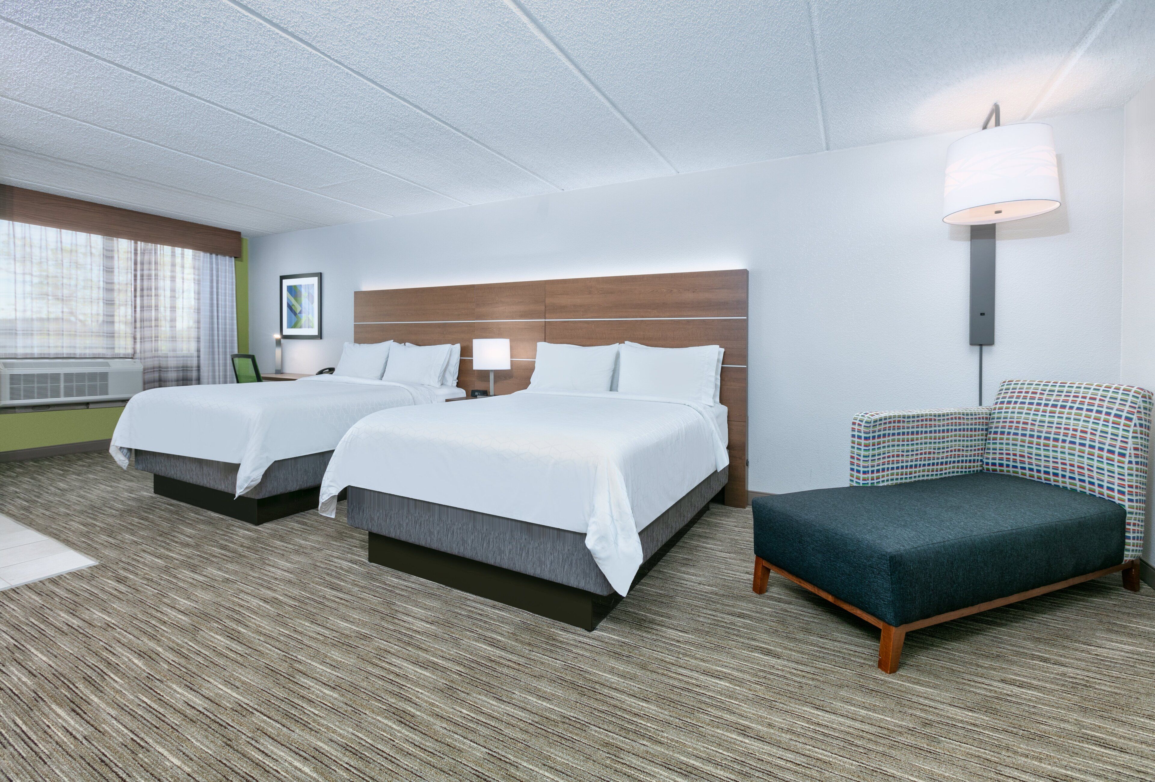 A hotel room with two beds, a desk, a chair, and a window with curtains.