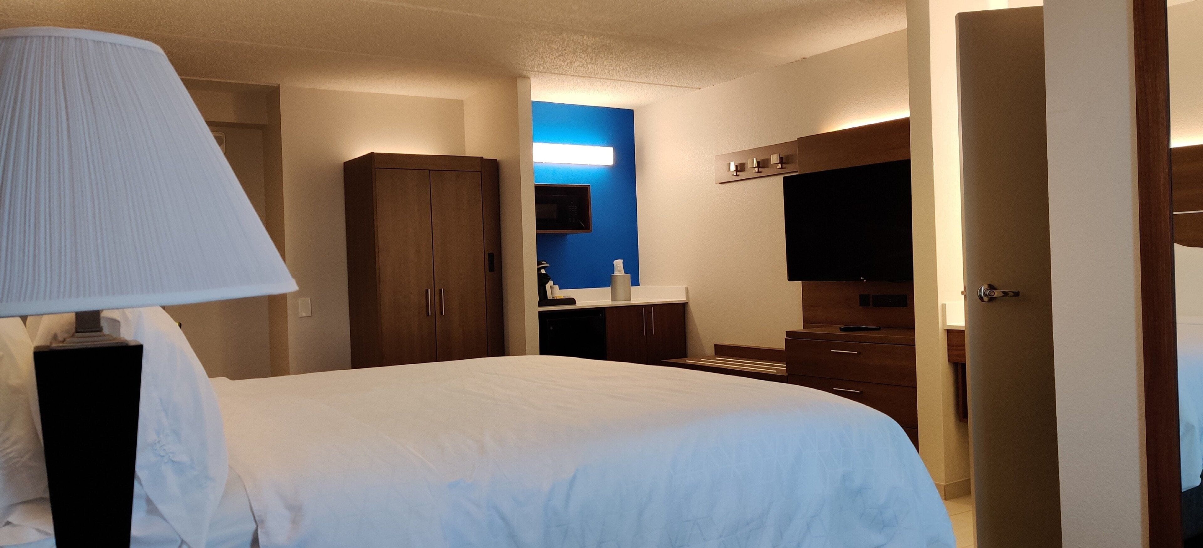 A hotel room with a bed, a nightstand, a lamp, a wardrobe, a TV, and a bathroom area.