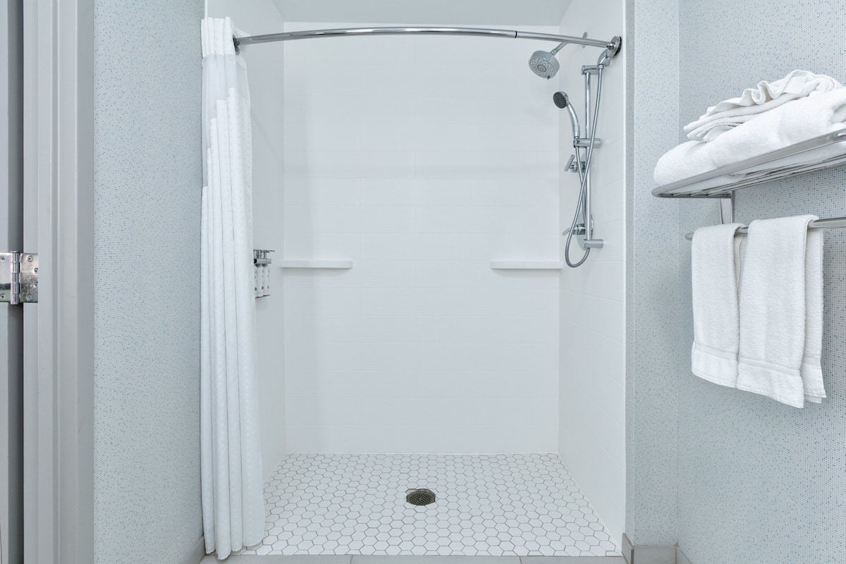 A shower with a curved door, a showerhead, and a tiled floor.