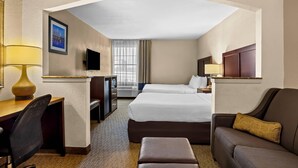 Habitación de hotel con escritorio, dos camas, sofá, televisor y ventana con cortinas.