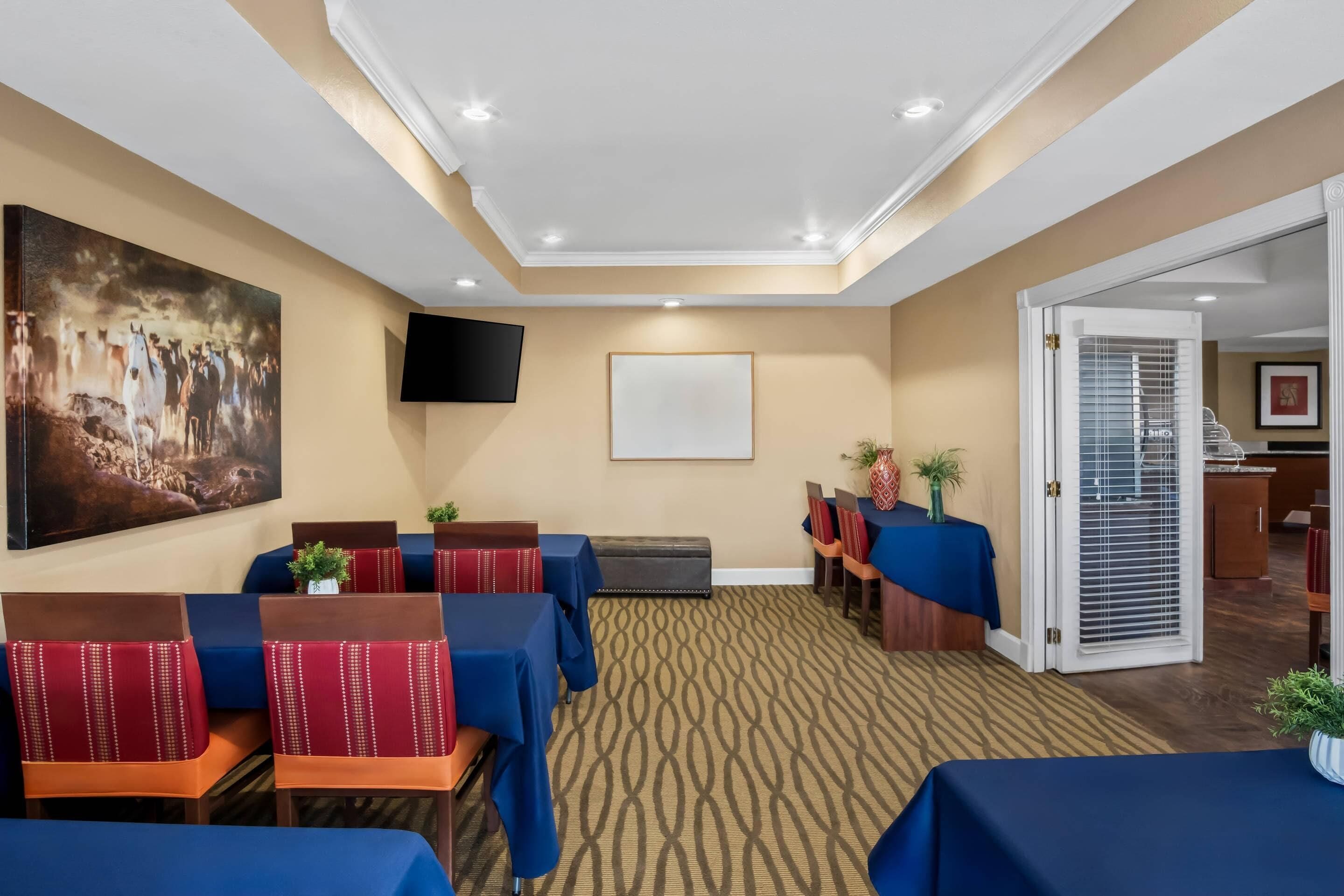 A conference room with tables and chairs, a large painting, a TV, and a patterned carpet.