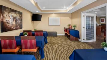 A conference room with tables and chairs, a large painting, a TV, and a patterned carpet.