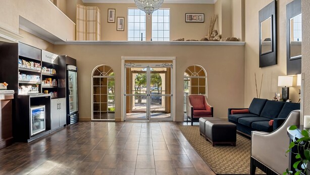 Un hall espacioso con techo alto, un candelabro, una zona de estar con sofá y sillones, una kitchenette y un gran ventanal que da al exterior.