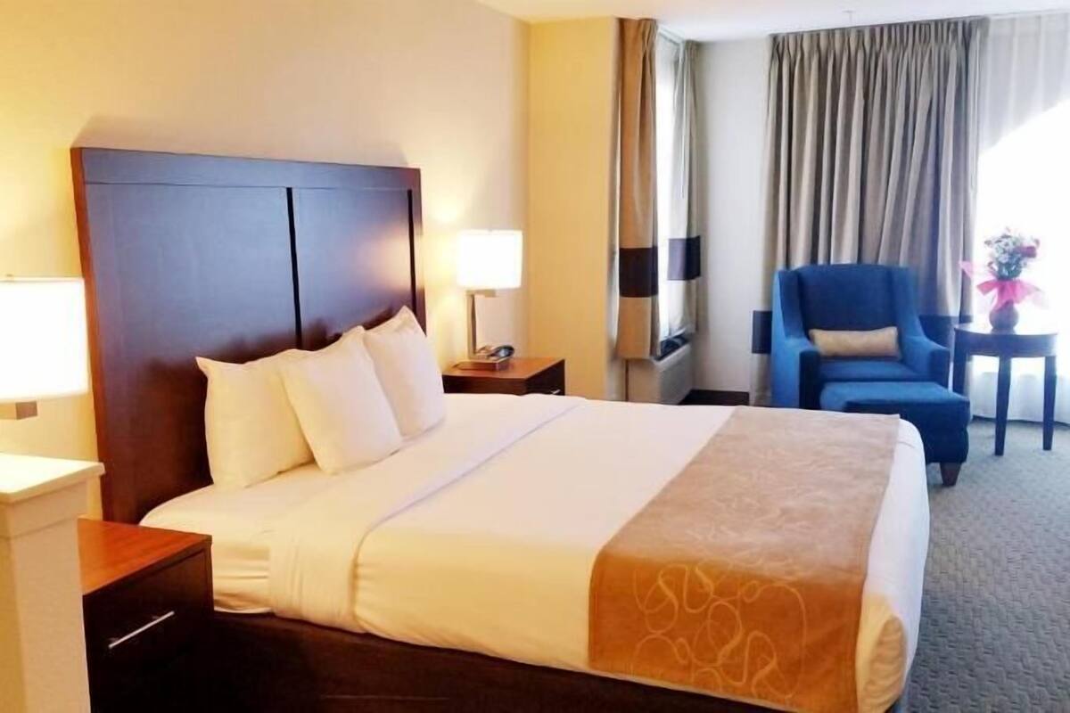 A hotel room with a large bed, two bedside tables with lamps, a chair, and a view of the outdoors.