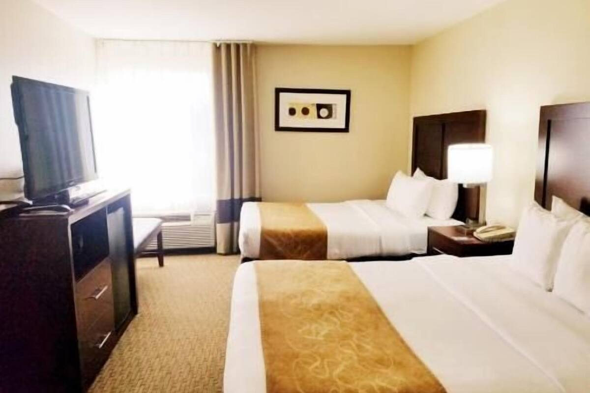 A hotel room with two beds, a television, a desk, and a framed picture on the wall.