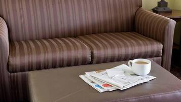 A brown striped sofa with a white cup and newspapers on a matching ottoman.