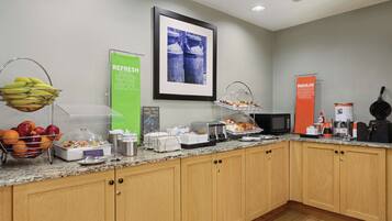 A breakfast bar with fruit, coffee, and pastries.