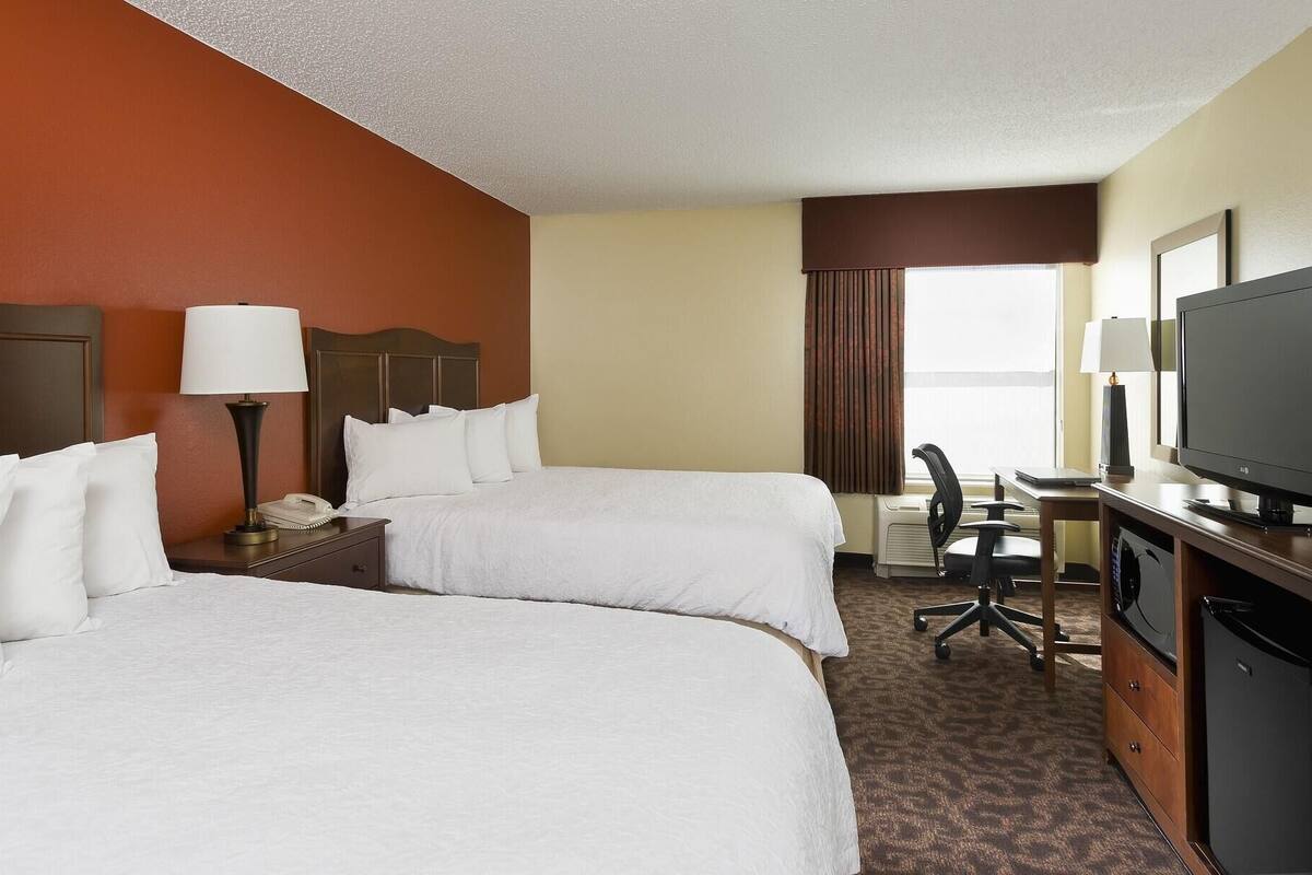 A hotel room with two beds, a desk with a computer, a television, and a desk lamp.