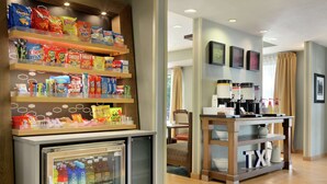 A hotel lobby with snack shelves, a refrigerator, a coffee station, and a bed in the background. - Hampton Inn San Angelo (San Angelo)