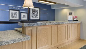 A reception desk with a granite countertop, wooden paneling, and framed black and white photographs on the wall. - Hampton Inn San Angelo (San Angelo)