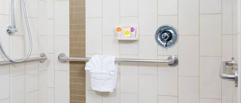A shower area with a handheld showerhead, a towel rack with a white towel, and a small shelf with soap bottles.