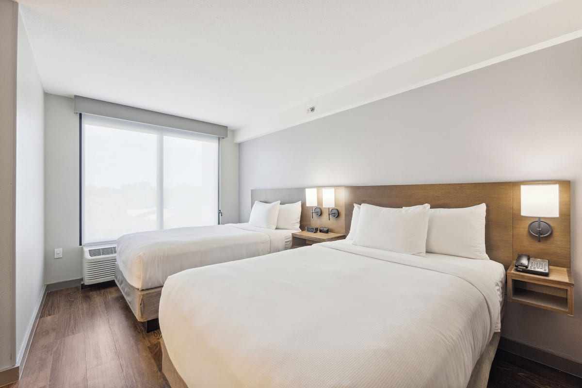 Une chambre d’hôtel avec deux lits, une grande fenêtre, un téléphone fixé au mur et une table de chevet.