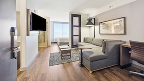 A modern living room with a grey sofa, a small round table, a standing lamp, and a flat-screen TV mounted on the wall. - Hyatt Place San Antonio-Northwest/Medical Center (San Antonio)