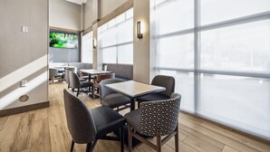 A modern dining area with wooden flooring, grey upholstered chairs, and large windows offering a view of the outdoors. - Hyatt Place San Antonio-Northwest/Medical Center (San Antonio)