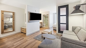 A modern living room with a flat-screen TV, a sofa, a coffee table, and a large mirror. - Hyatt Place San Antonio-Northwest/Medical Center (San Antonio)