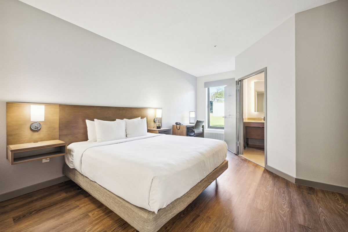 Une chambre d’hôtel moderne dotée d’un grand lit, d’une tête de lit en bois, de tables de chevet et offrant une vue sur l’extérieur.