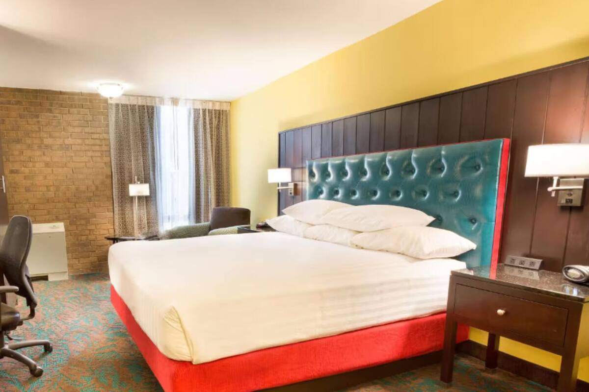 Ein Hotelzimmer mit einem großen Bett, einem Schreibtisch mit Stuhl, einem kleinen Tisch und einer Wandleuchte.