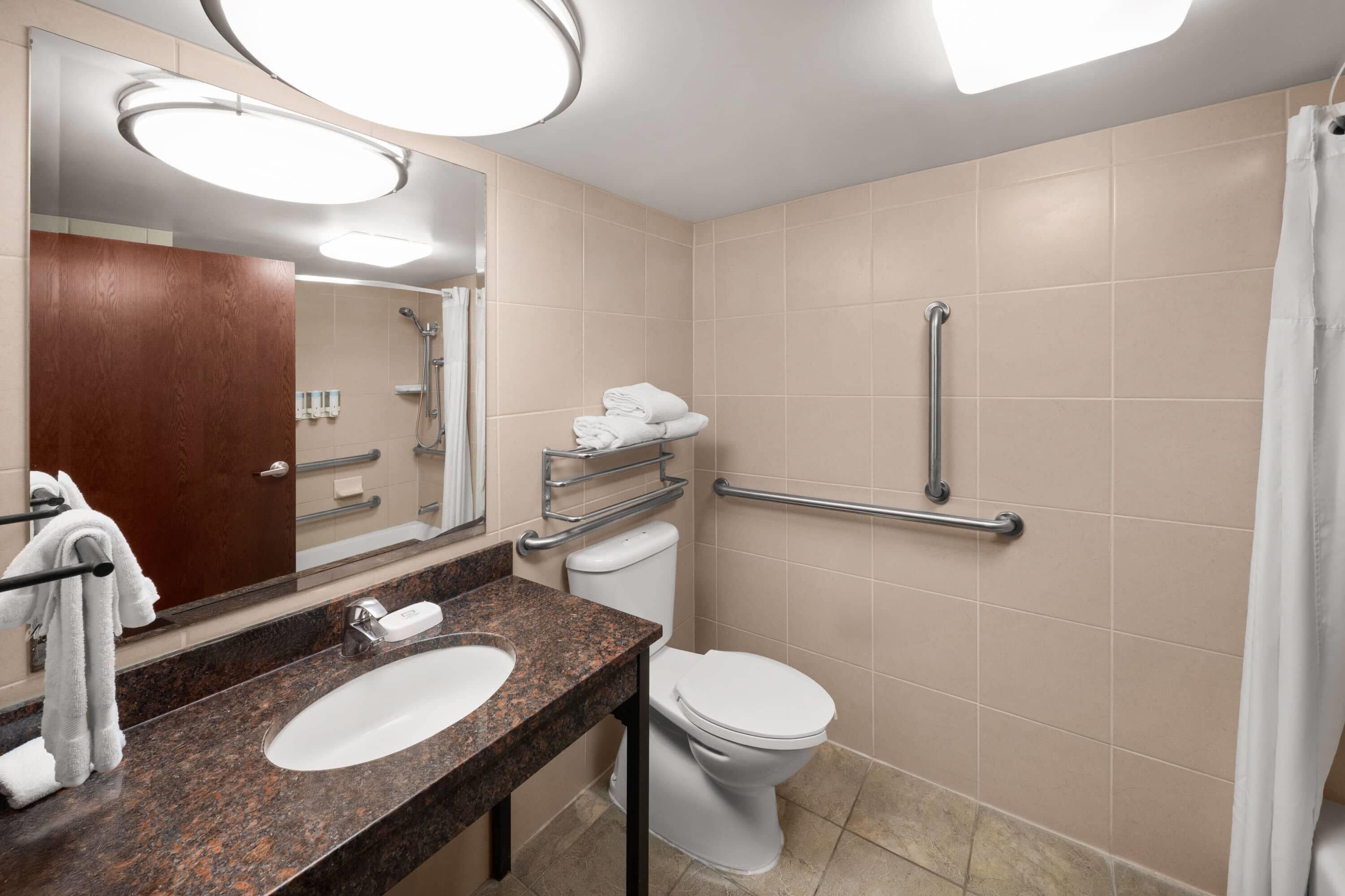 A bathroom with a sink, mirror, toilet, and grab bars.