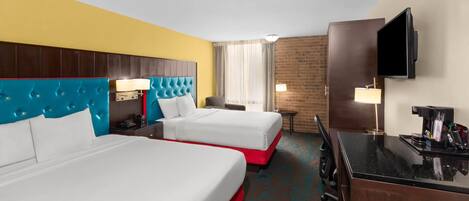 A hotel room with two beds, a desk, a TV, and a coffee machine.