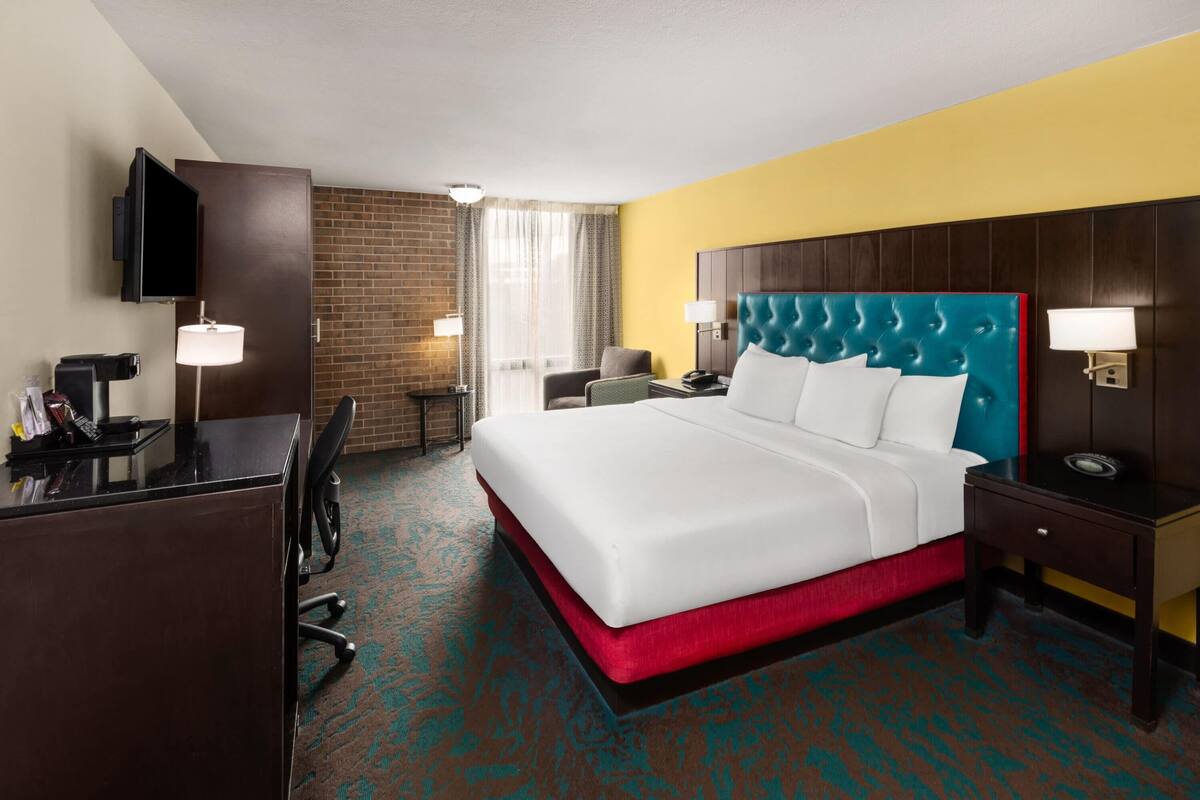 Ein Hotelzimmer mit einem großen Bett, einem Schreibtisch mit Stuhl, einem Fernseher und einer Ziegelwand.