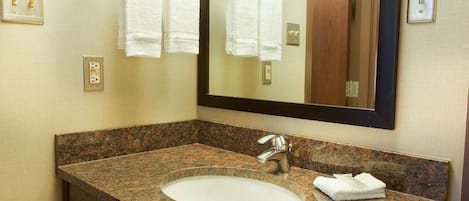 Un baño con lavamanos de granito, un espejo y dos toallas blancas colgadas en un perchero.