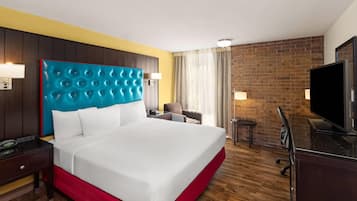 Une chambre d’hôtel avec un grand lit, une télévision, un bureau avec une lampe et un mur en briques.