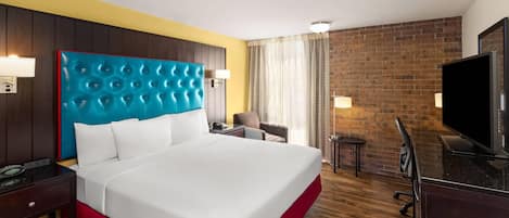 Ein Hotelzimmer mit einem großen Bett, einem Fernseher, einem Schreibtisch mit Lampe und einer Ziegelwand.