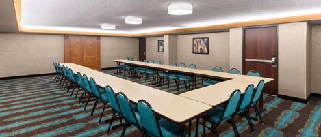 A conference room with a long table, chairs, carpeted floor, wooden door, and framed pictures on the wall.