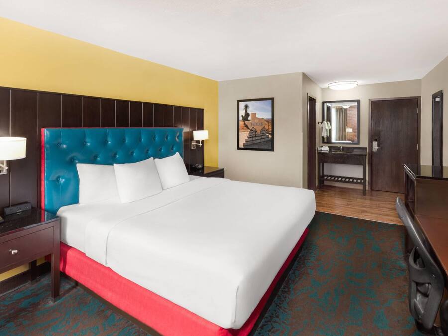 Habitación de hotel con cama, mesita de noche, lámpara y espejo.