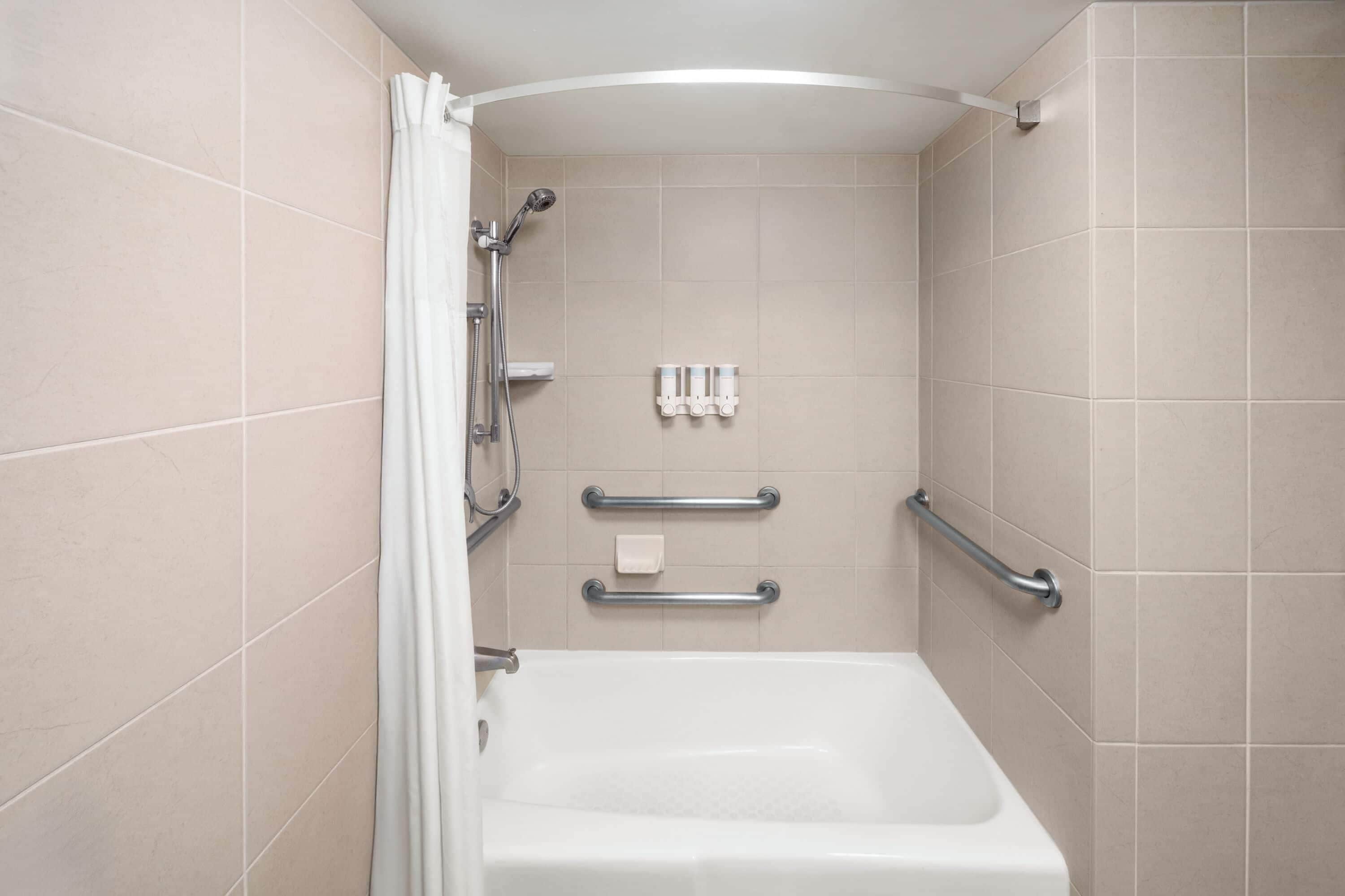A bathroom with a bathtub, grab bars, and a showerhead.