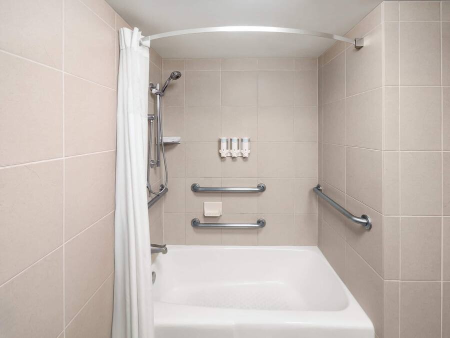 A bathroom with a bathtub, grab bars, and a showerhead.