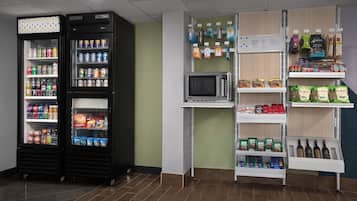 A self-service kiosk area with refrigerated beverage dispensers, a microwave, and shelves stocked with snacks, beverages, and packaged goods.