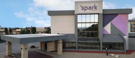 A modern hotel building with a 'spark by Hilton' sign, featuring a large glass entrance and a unique geometric facade.