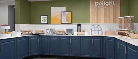 A modern kitchen with dark blue cabinets, white countertops, and a green accent wall. There are various appliances and kitchenware on the counter.