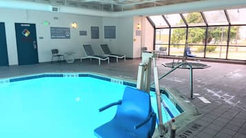A swimming pool with safety signs, lounge chairs, and a view of the outdoors through large windows.