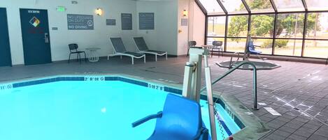 A swimming pool with safety signs, lounge chairs, and a view of the outdoors through large windows.