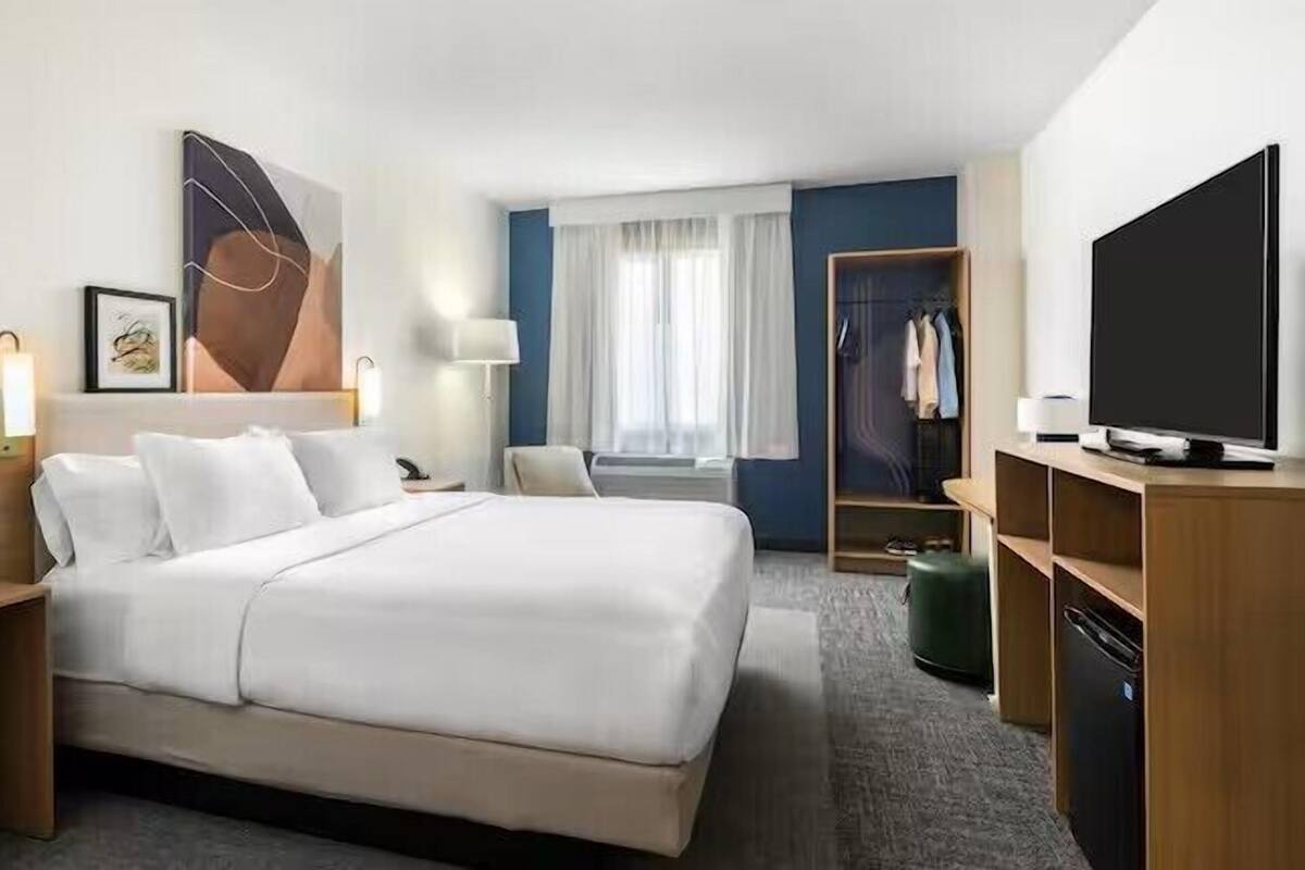 Ein Hotelzimmer mit einem großen Bett, Nachttischen, einem Fernseher, einem Kleiderschrank und einem Fenster mit Vorhängen.