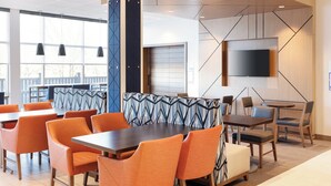 A modern dining area with orange chairs, a patterned booth, and a flat-screen TV mounted on the wall. - Holiday Inn Express - Layton by IHG (Layton)