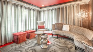 Une chambre d’hôtel moderne avec un canapé incurvé, des poufs rouges, un fauteuil blanc et un lustre.