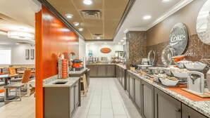 Un espace cuisine moderne doté d’un long comptoir, de divers appareils électroménagers et d’un coin repas avec des tables et des chaises.