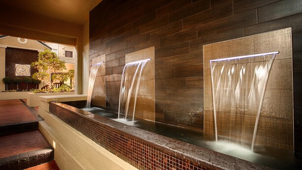Un aménagement aquatique intérieur moderne, avec trois cascades descendant le long d’un mur en bois, entouré d’un espace banc avec des carreaux décoratifs.