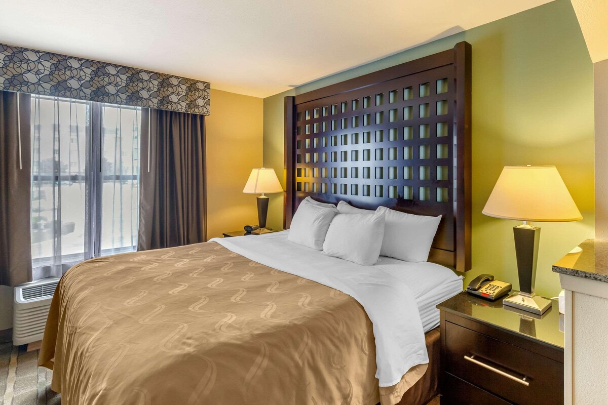 A hotel room with a large bed, two bedside tables with lamps, a telephone, and a window with curtains.